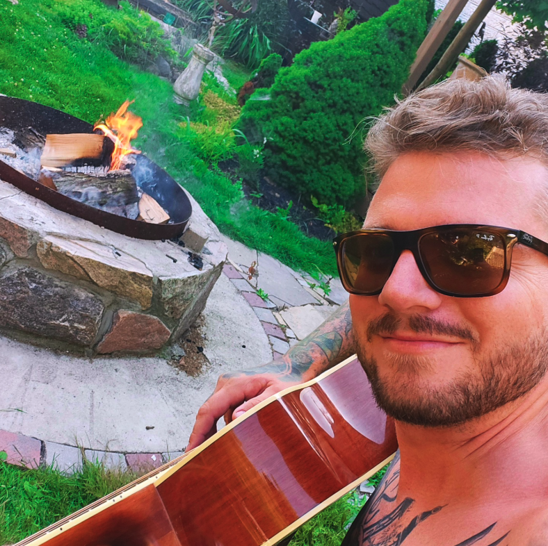 Sons Command owner sitting with a guitar beside a backyard fire